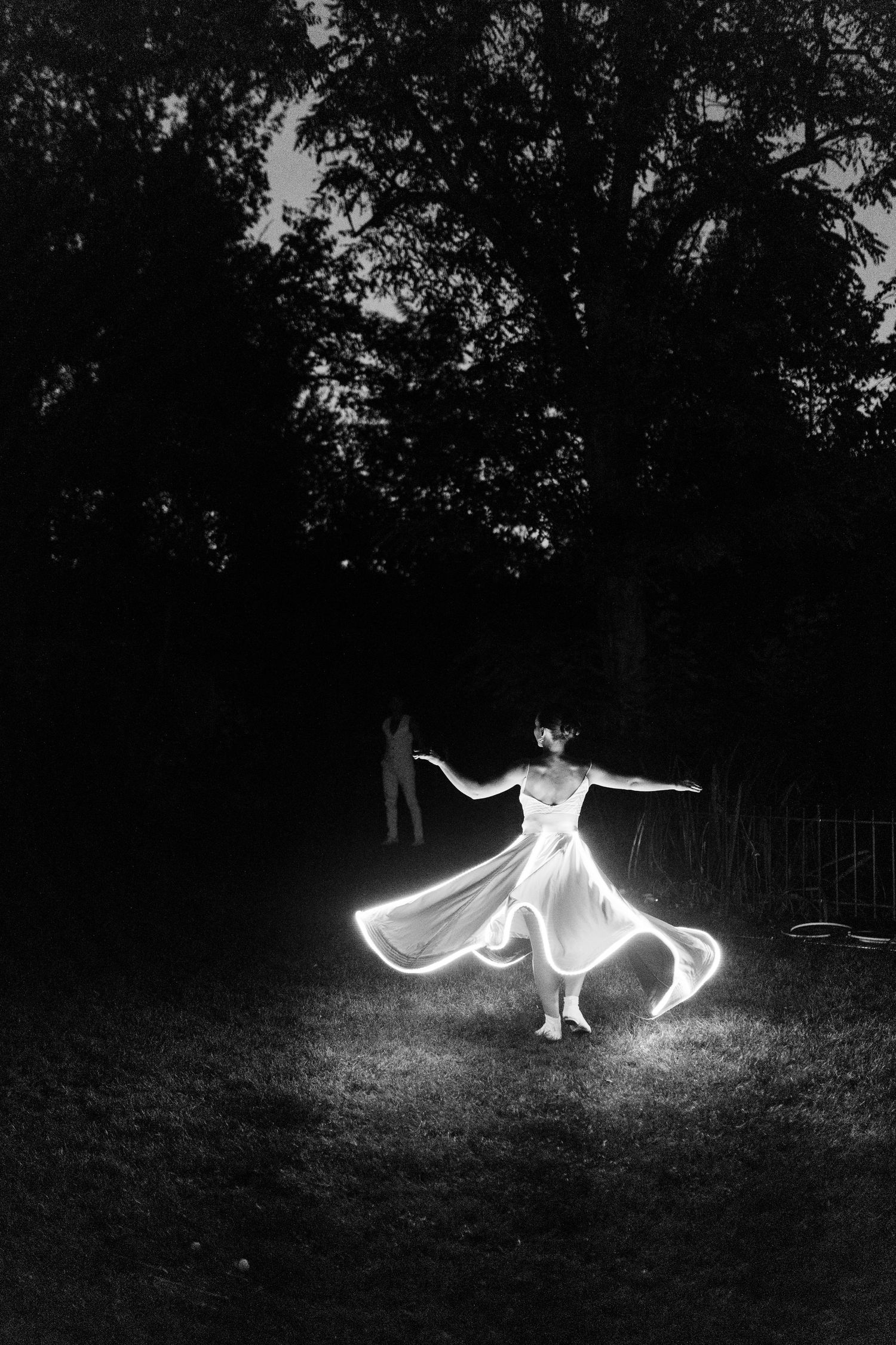 Black and white photo of bride twirling in wedding dress with light painting effect at night outdoors.