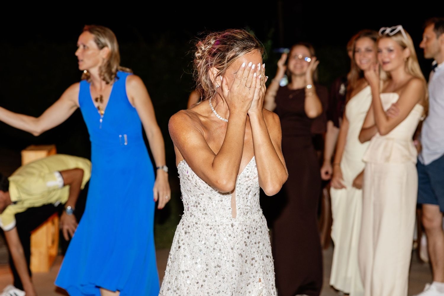 Bride covering face with hands laughing during outdoor evening wedding reception dance party.