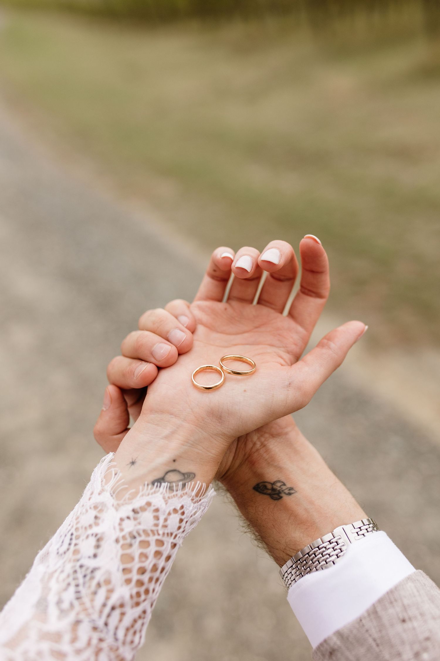Couple displays two gold wedding rings resting on bride's palm with lace sleeve detail.