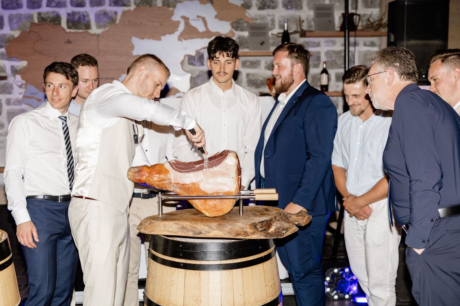 Chefs and guests gather around a whole roasted ham being carved at an elegant event.