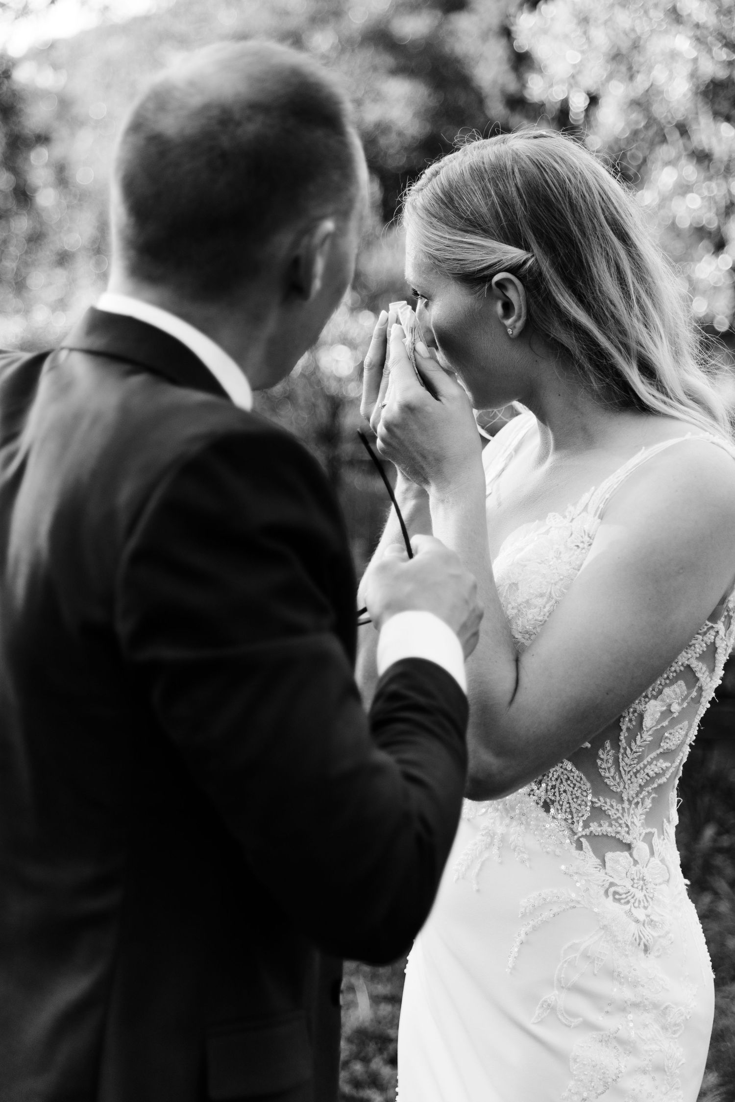 Black and white photo of emotional bride wiping tears during wedding ceremony while groom stands close.