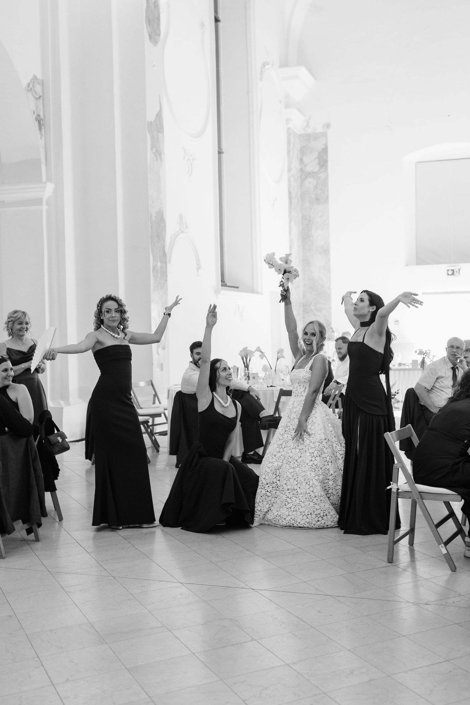 Black and white photo of bride and bridesmaids in black gowns celebrating joyfully at wedding reception.