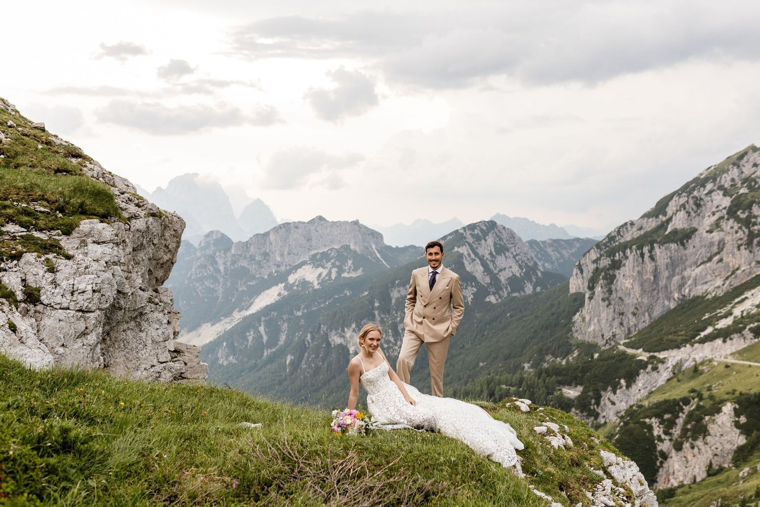 Bride and groom celebrate on a scenic Alpine mountain ridge with dramatic peaks and valleys in the background.