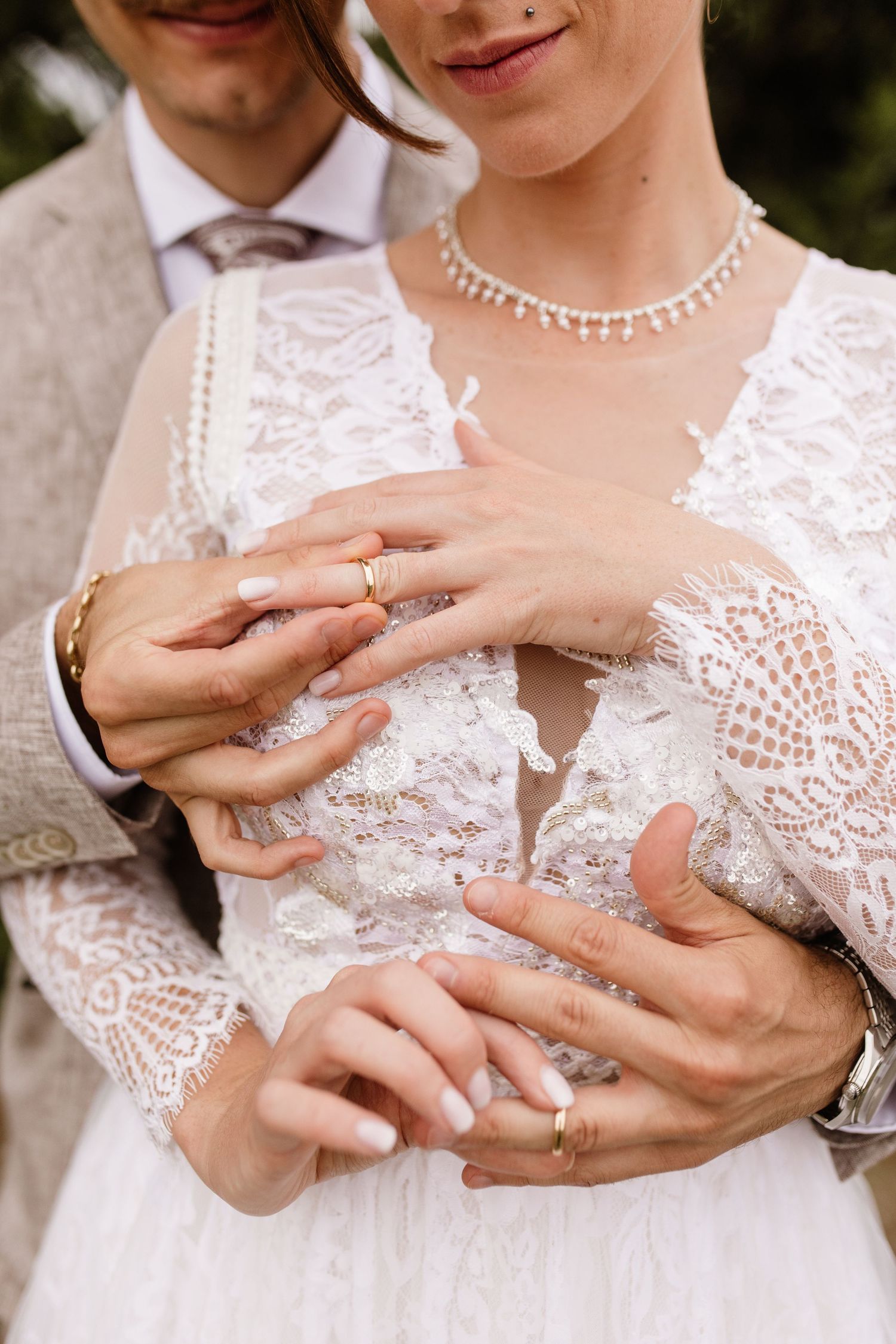 Newlyweds show off gold wedding rings as groom embraces bride in intricate lace gown.