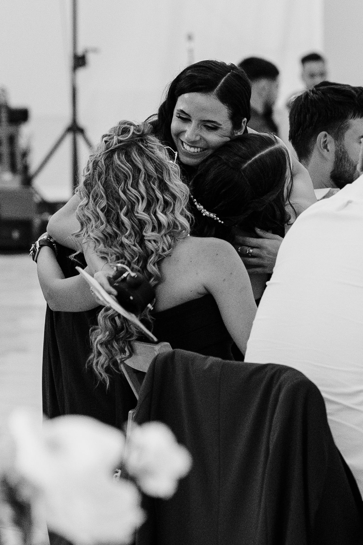 Black and white photo of women sharing a warm embrace and smiling at a wedding reception event.