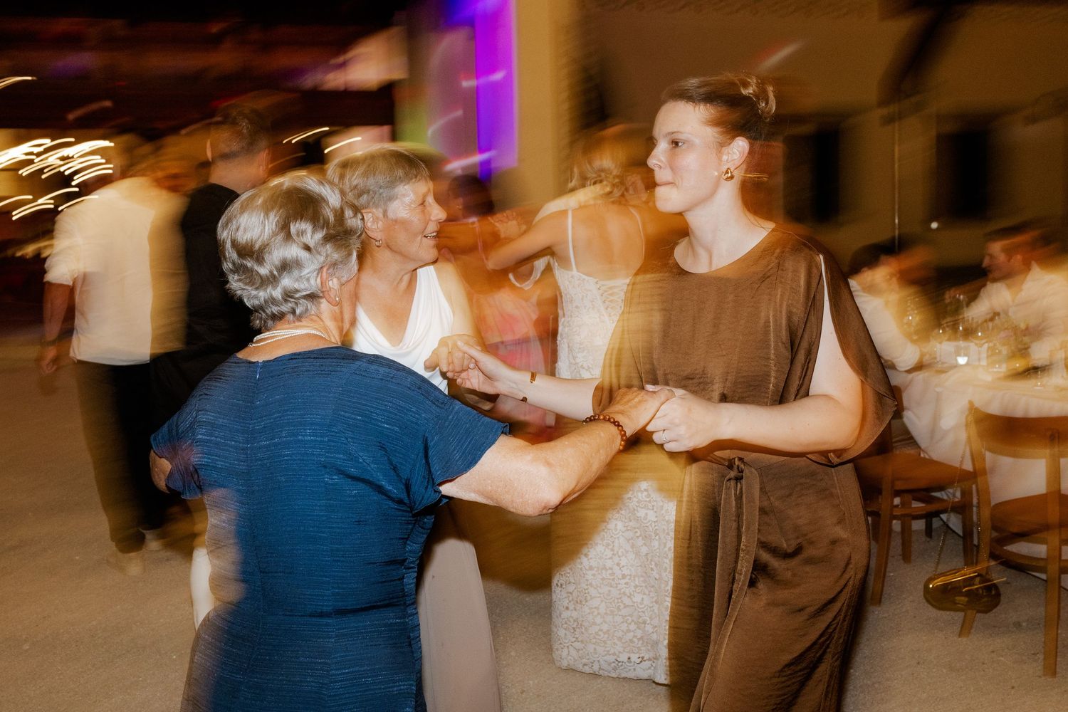 Guests dancing joyfully at wedding reception with motion blur capturing the energy of the celebration indoors.