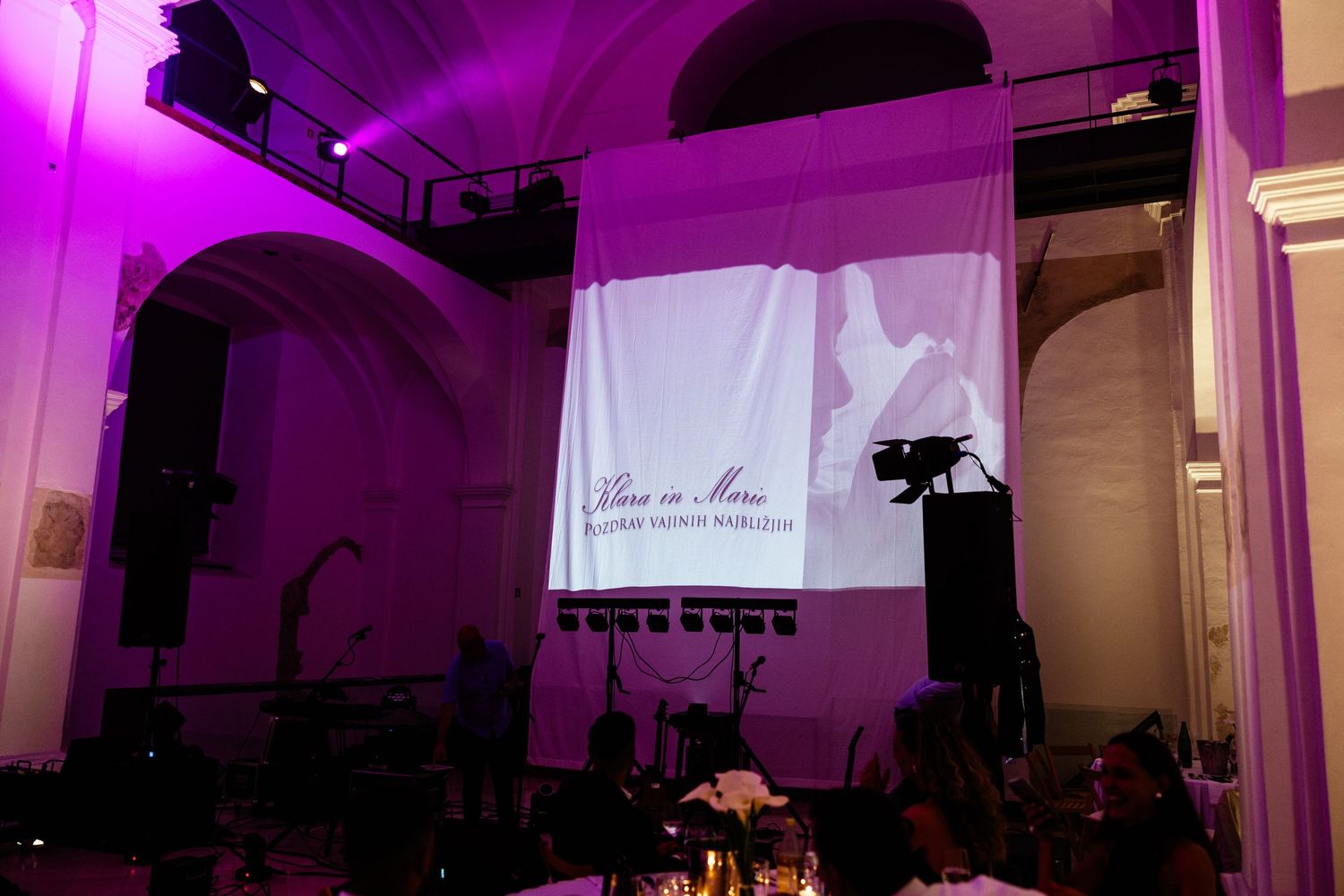 Wedding reception venue with purple lighting and couple's name projected on large screen.