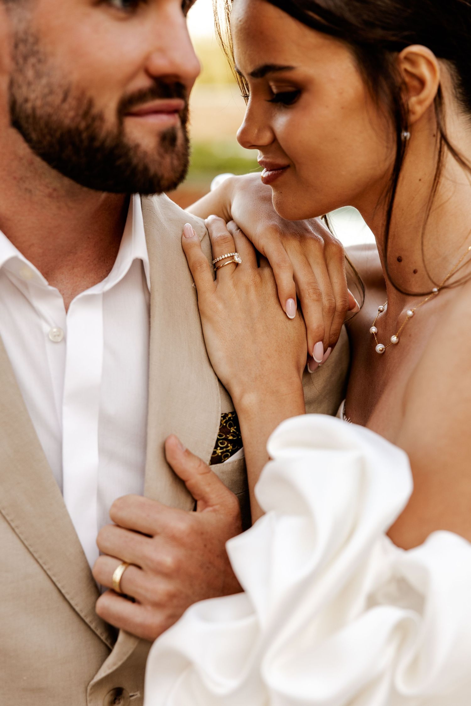 Close-up of a bride and groom sharing an intimate moment, showcasing gold wedding rings and elegant bridal accessories.