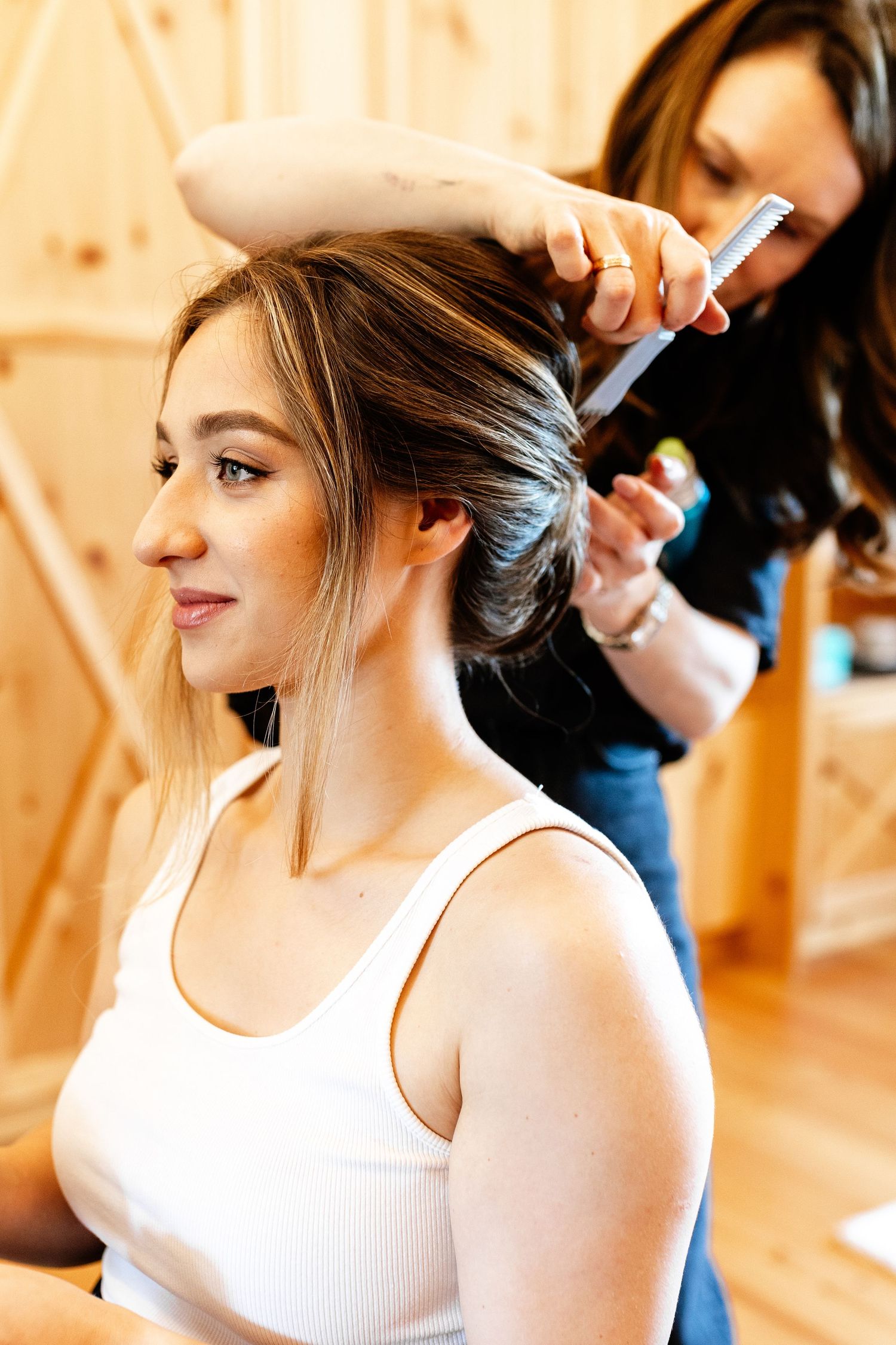 A hairstylist carefully styling a young woman's hair in a bright wooden salon setting.