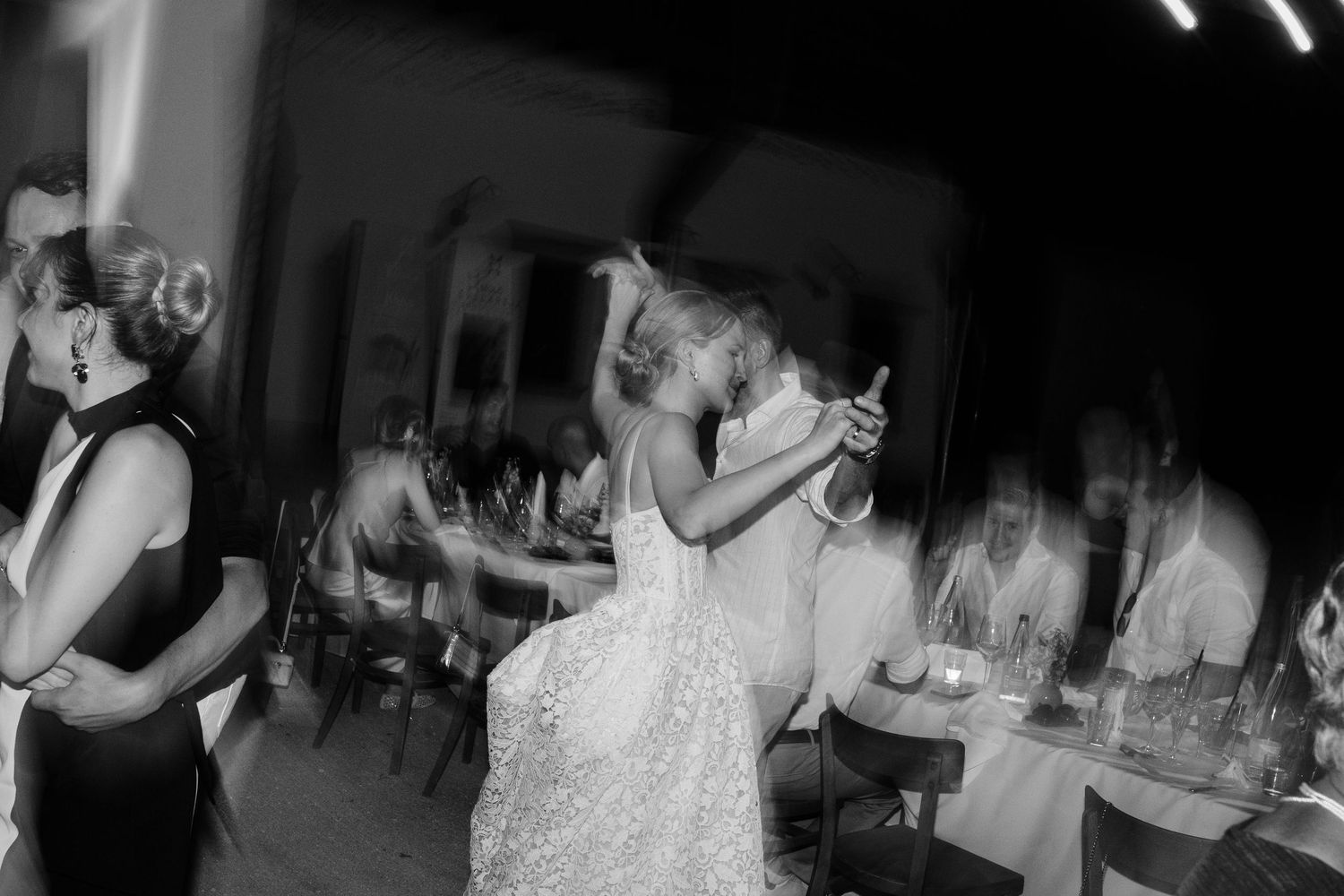 Bride dances joyfully with a guest in a blurred motion black and white wedding reception photo.