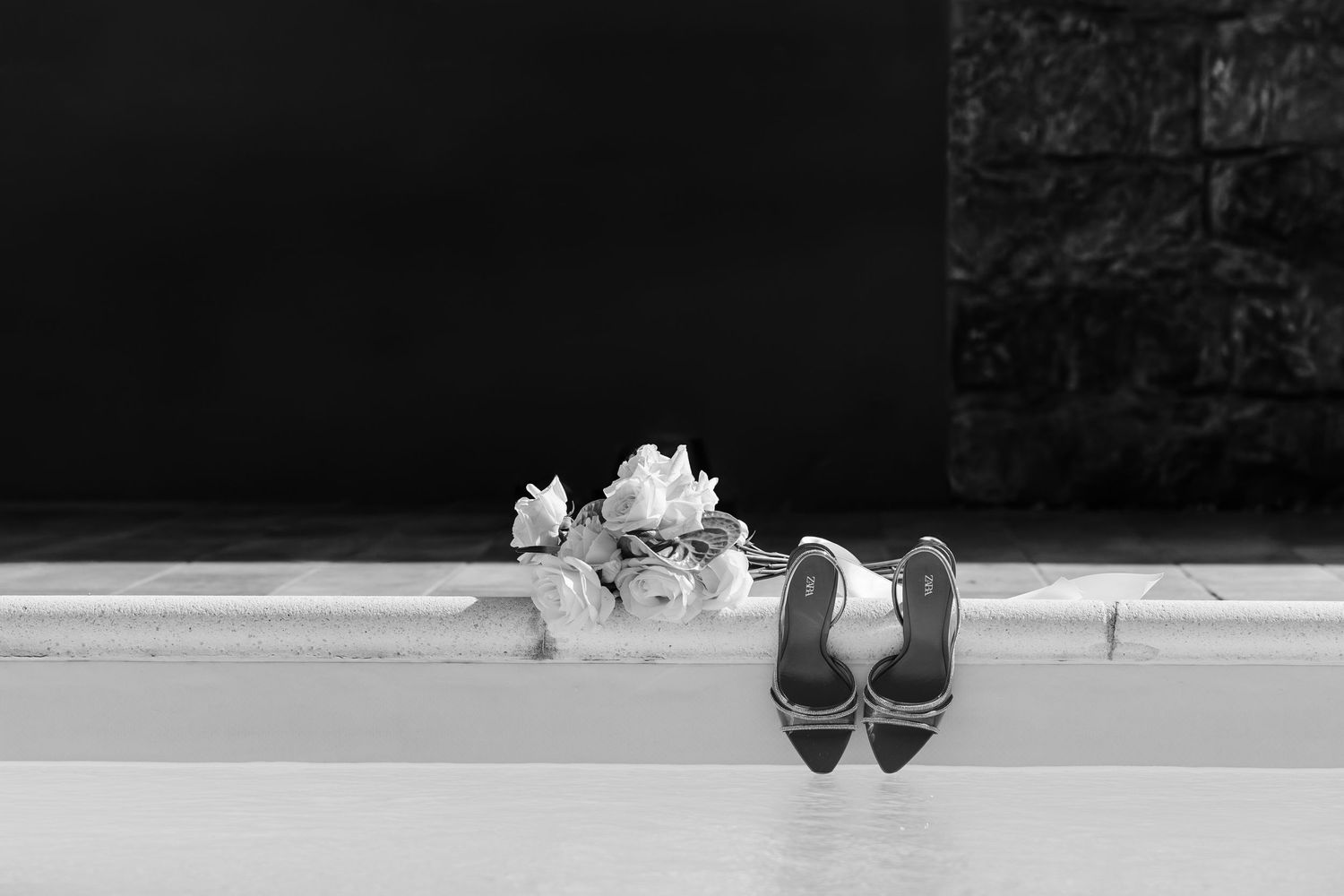 Black and white photo of bridal heels and white flowers on steps outdoors.