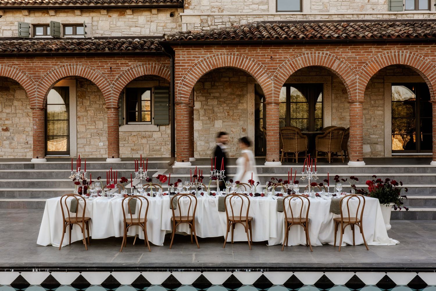 Elegant outdoor wedding reception table set under brick arches in a Tuscan courtyard with white linens.
