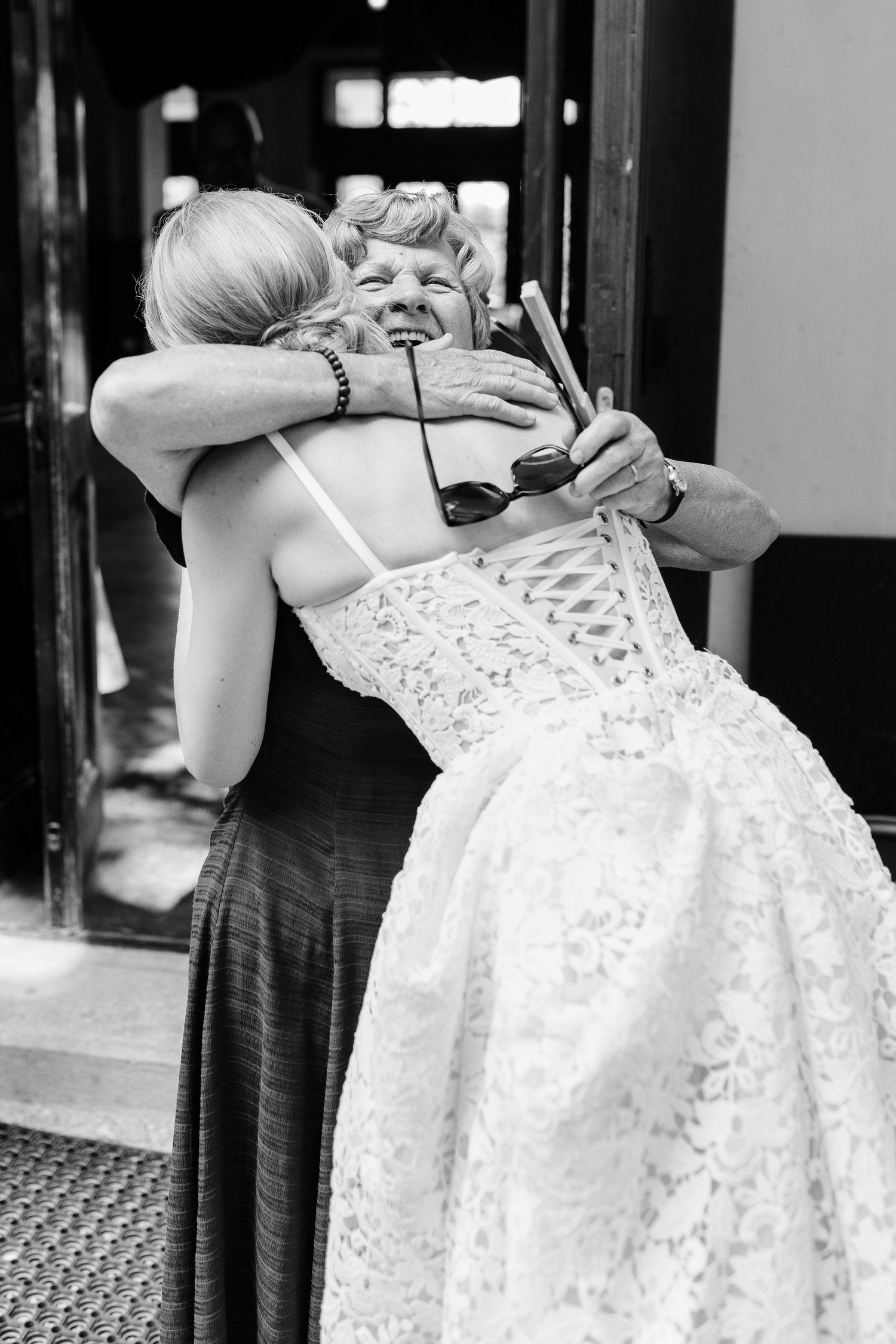 Bride and elderly woman share an emotional hug in black and white wedding photo.