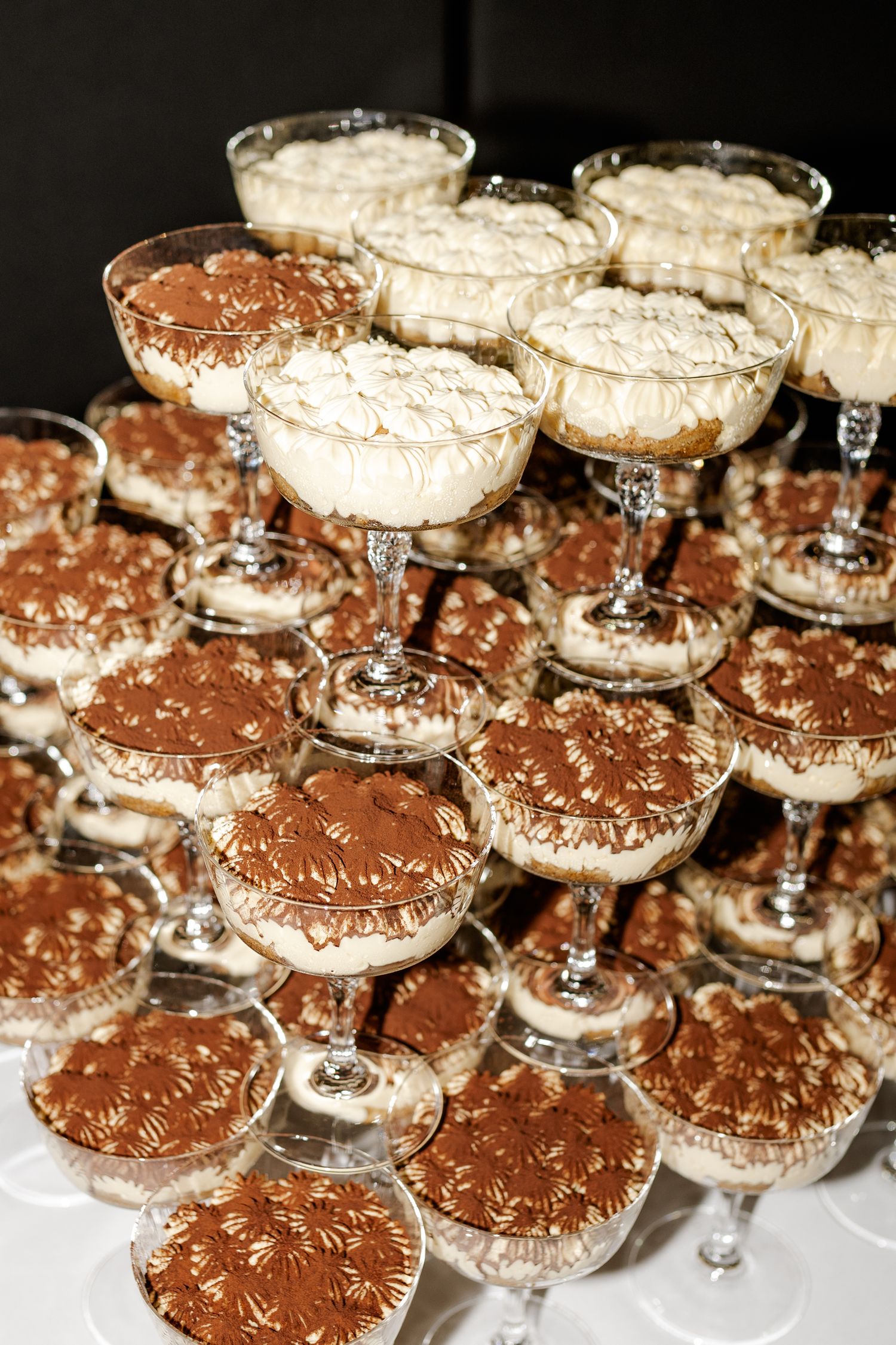 Elegant pyramid display of tiramisu desserts served in crystal champagne coupe glasses at a formal event.