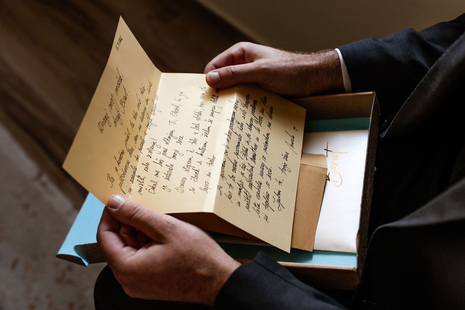 Person holding an open handwritten letter on aged paper, with more letters visible in a box below.