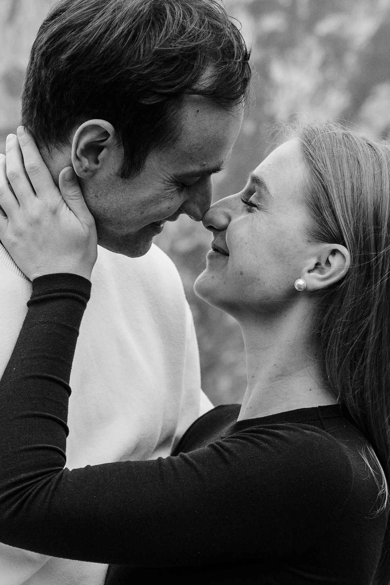 Black and white photo of a romantic couple about to kiss, woman holding man's face tenderly.