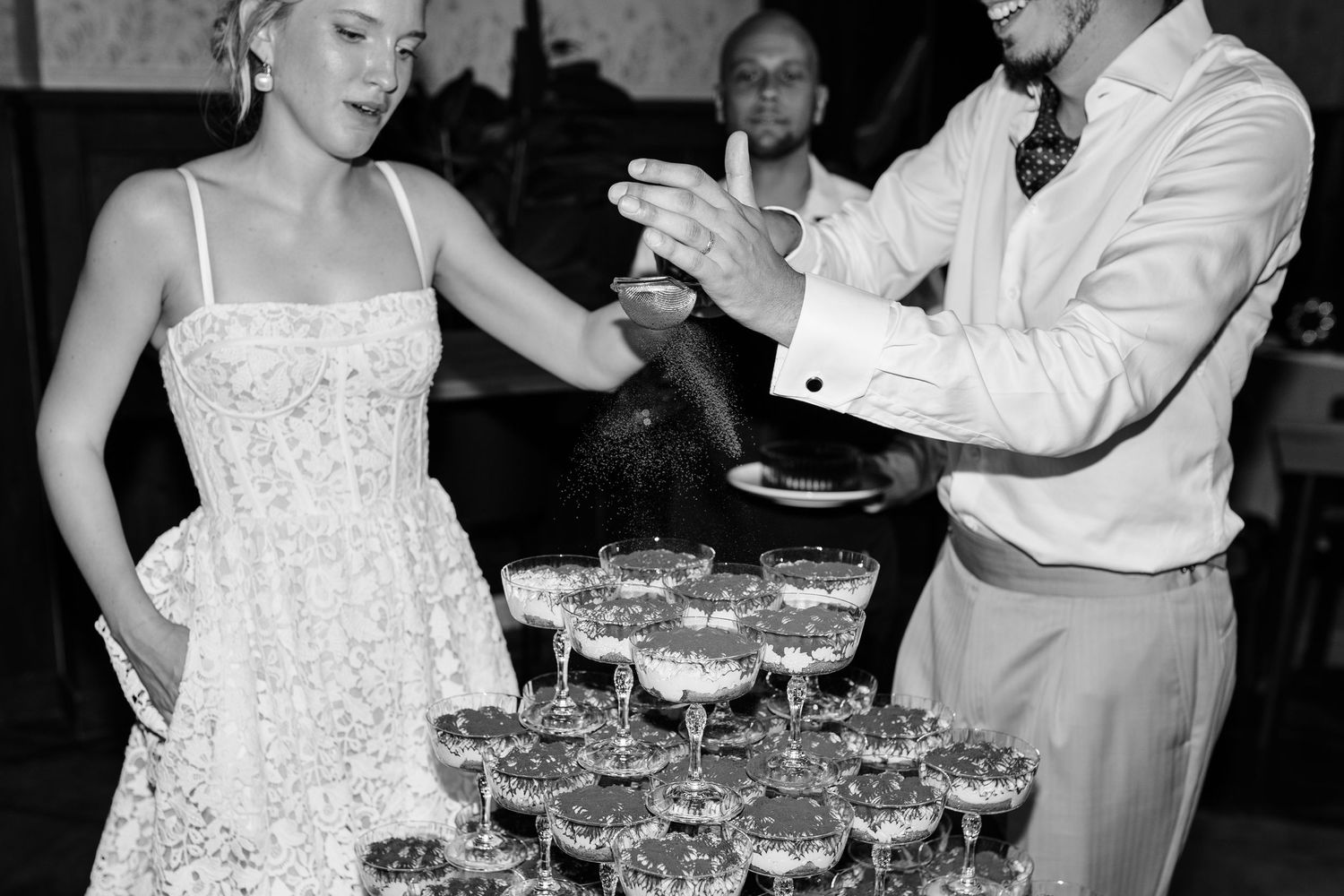 Black and white photo of a couple pouring champagne tower at a wedding reception celebration.