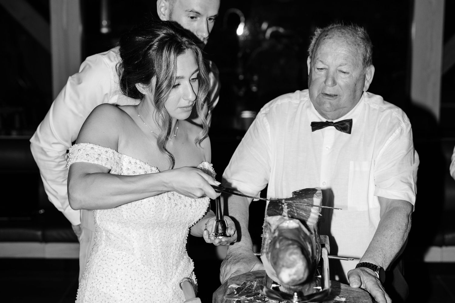 Bride and older gentleman examine vintage motorcycle at black and white wedding reception.