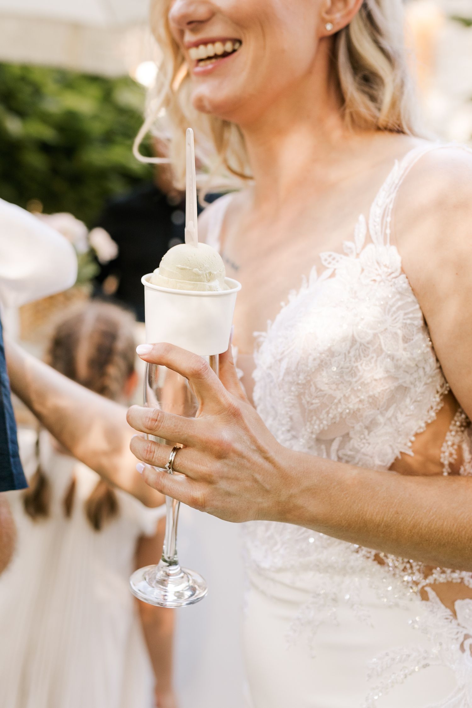 Smiling bride in lace gown holding an elegant champagne flute with sorbet and straw at wedding reception.