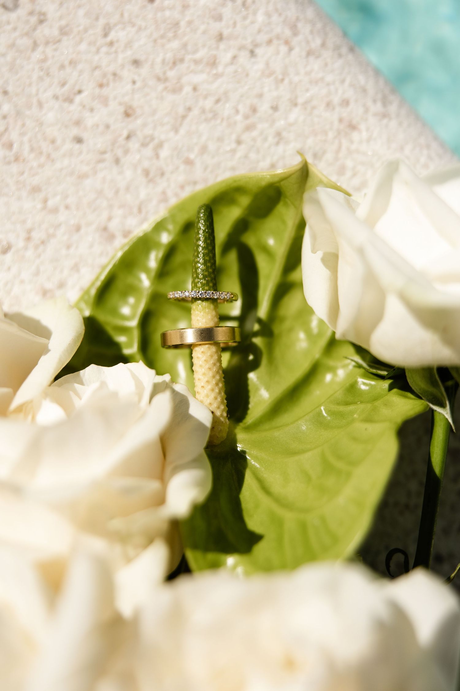 Gold wedding rings and diamond cross nestled among white roses and green leaves.