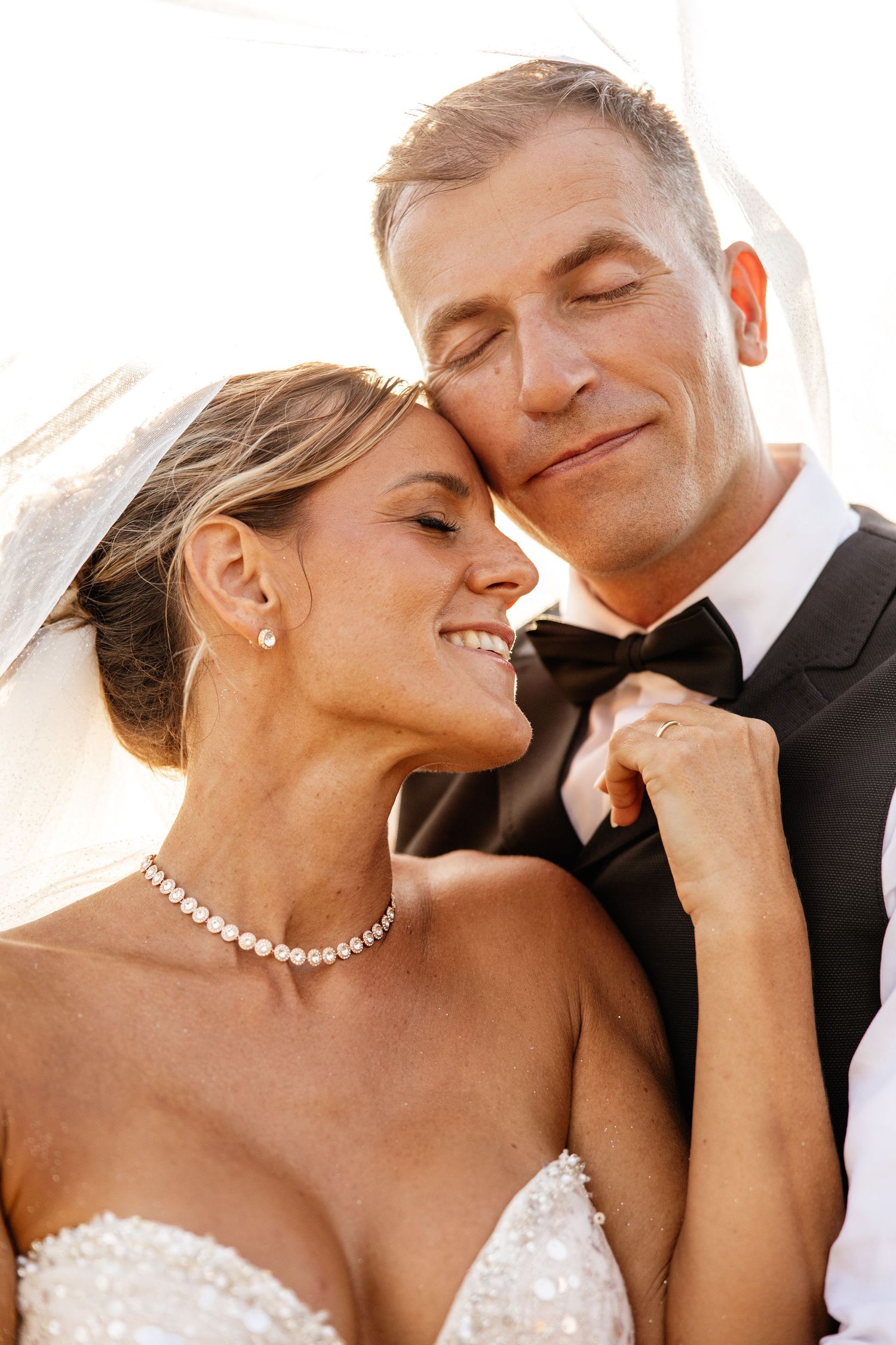 Close-up portrait of smiling bride and groom in wedding attire sharing a tender romantic moment.