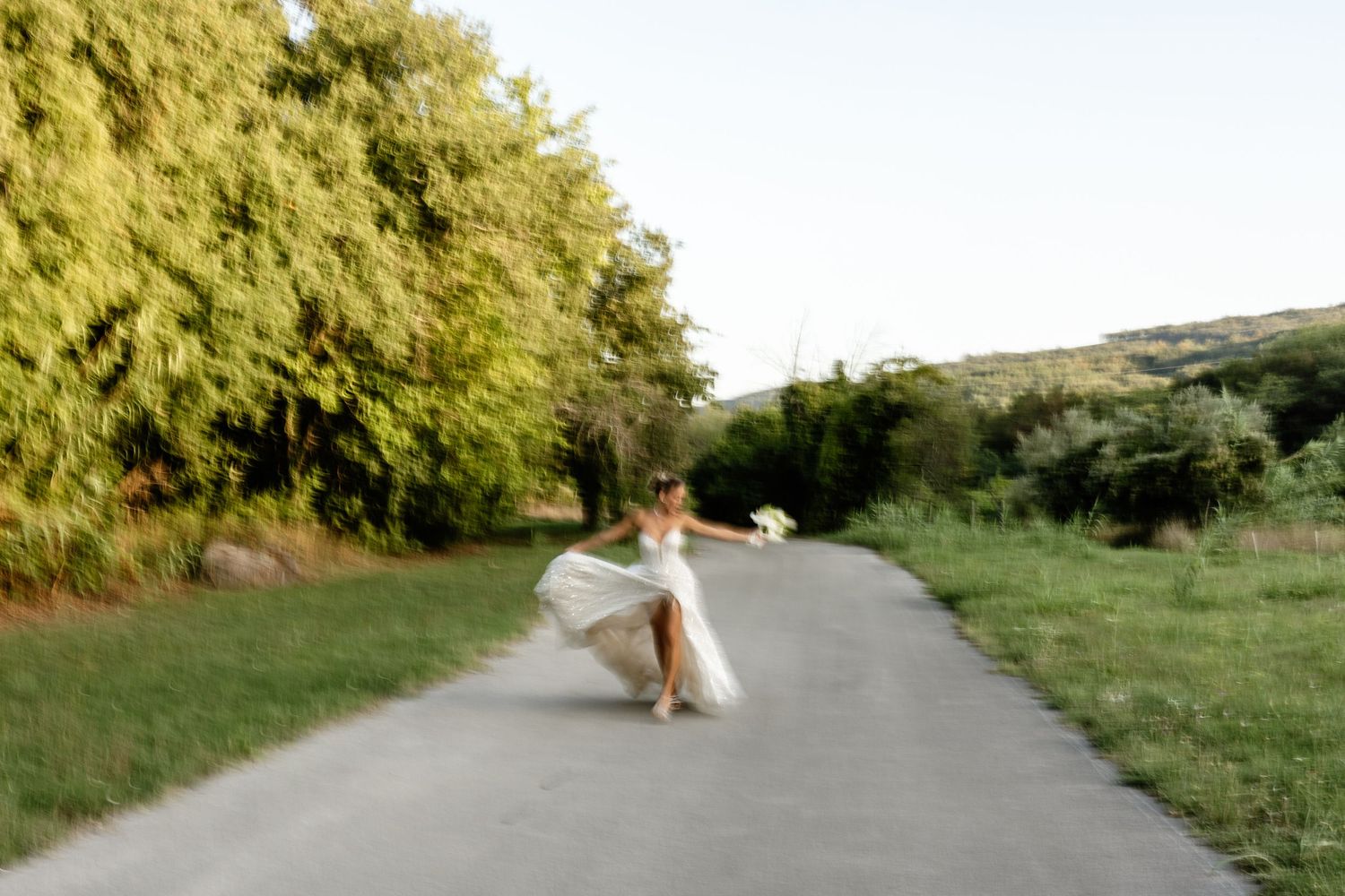 Bride twirls in her flowing white gown on a scenic rural road surrounded by lush greenery.