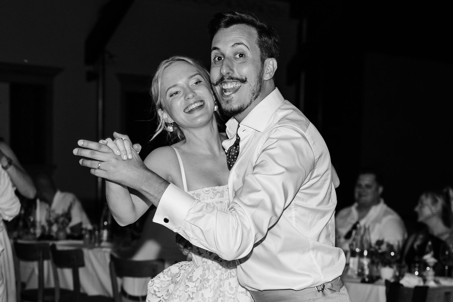 Bride and groom share a joyful first dance at their wedding reception in black and white photo.