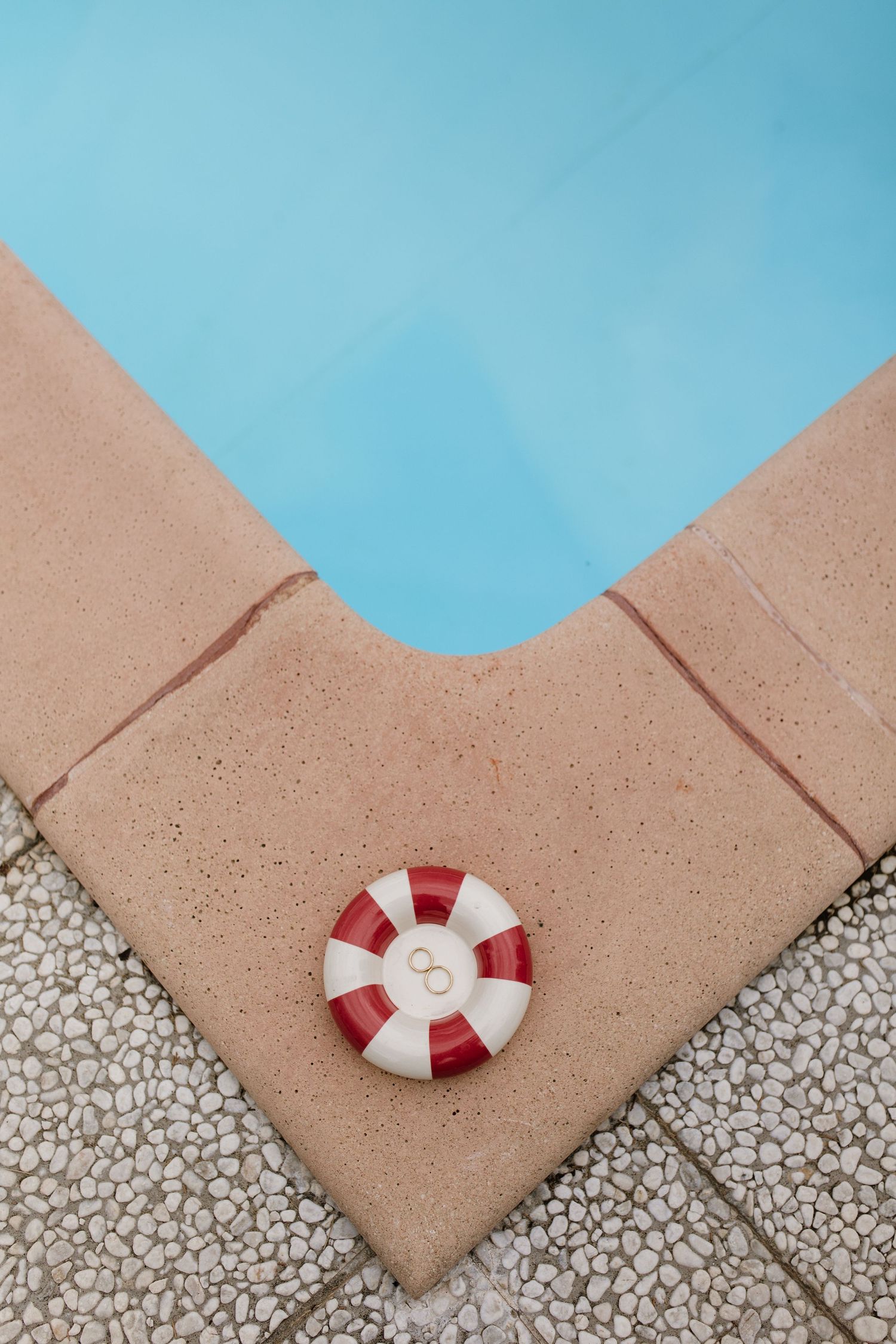 Red and white life preserver ring on pool edge corner with blue water, aerial view.