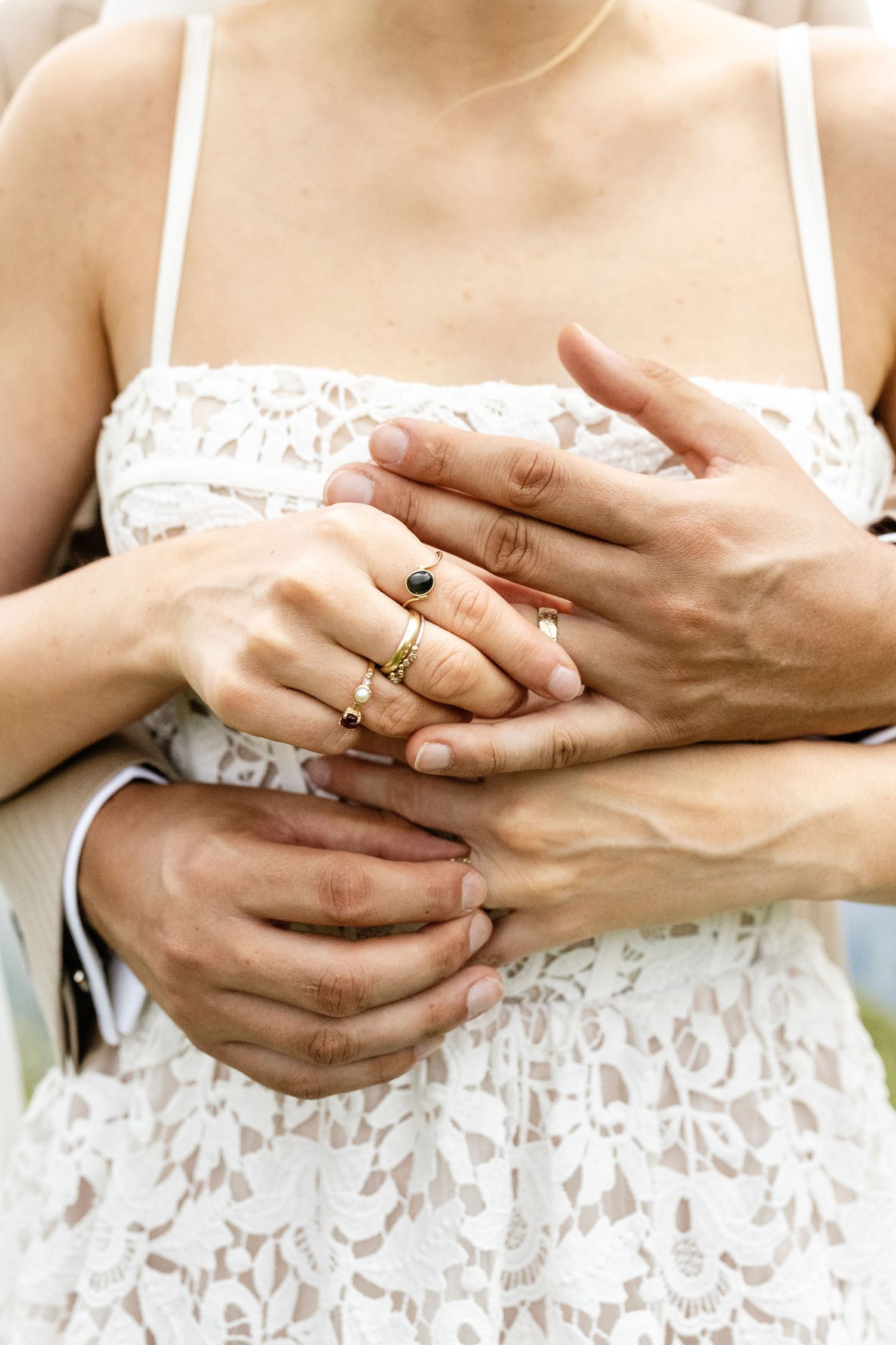 Close-up of couple's hands embracing, bride wearing gold rings on white lace wedding dress.