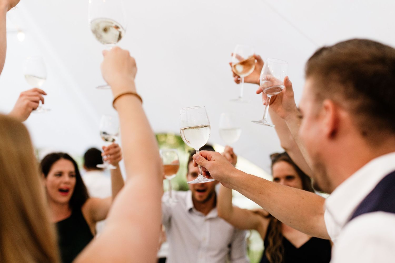 Guests raising champagne glasses in a celebratory toast at a wedding reception under a white tent.