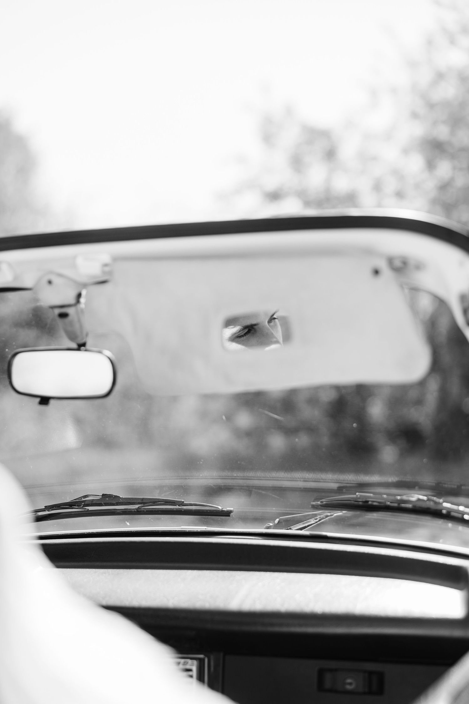 Black and white interior view of a vintage car dashboard with windshield wipers and rearview mirror.