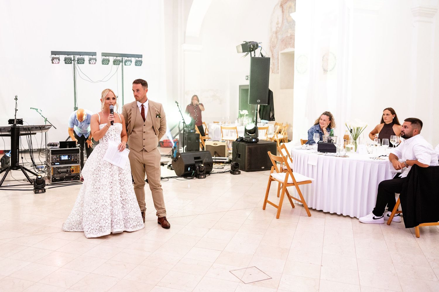 Bride and groom sharing first dance in elegant white venue while wedding guests watch and celebrate.