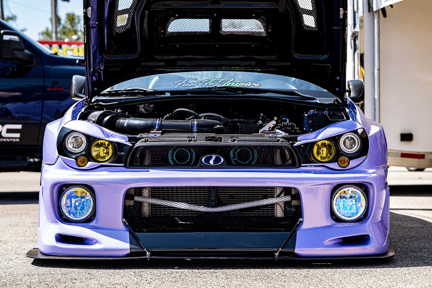 Purple widebody Subaru Impreza WRX STI with yellow fog lights and open hood at car show. Holley LS Fest