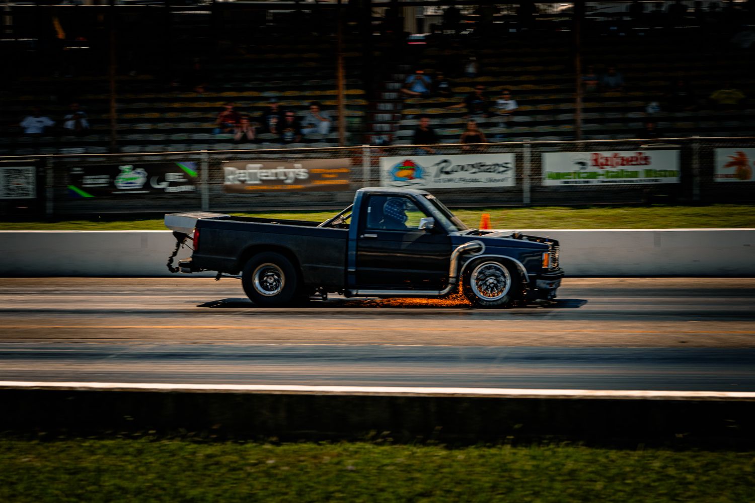 Black pickup truck racing at high speed on a drag strip at dusk with motion blur. Holley LS Fest