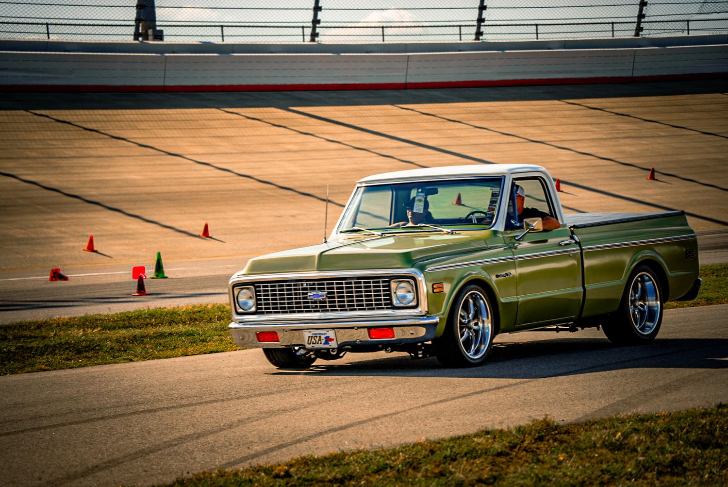 Classic olive green Chevrolet C10 pickup truck driving on racetrack with orange cones. C10 Nationals Nashville
