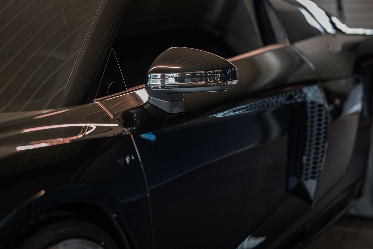 Close-up of sleek black sports car side mirror with carbon fiber accents in garage. Street Car Takeover