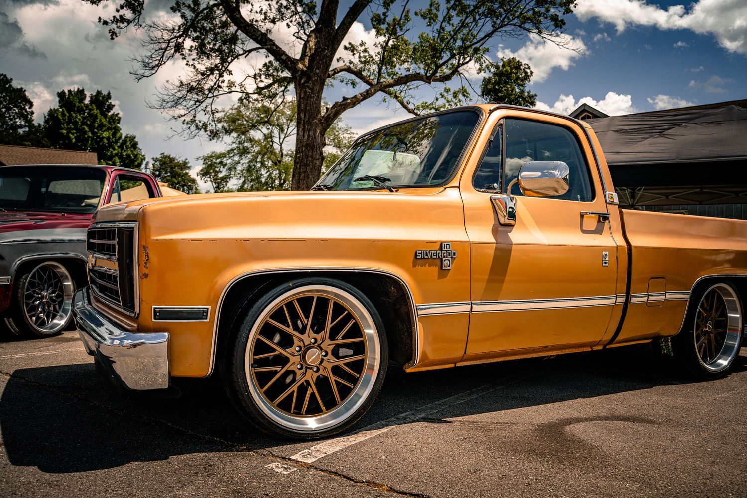 Orange lowered classic GMC C10 pickup truck with gold spoke wheels at outdoor car show. Southeastern Truck Nationals