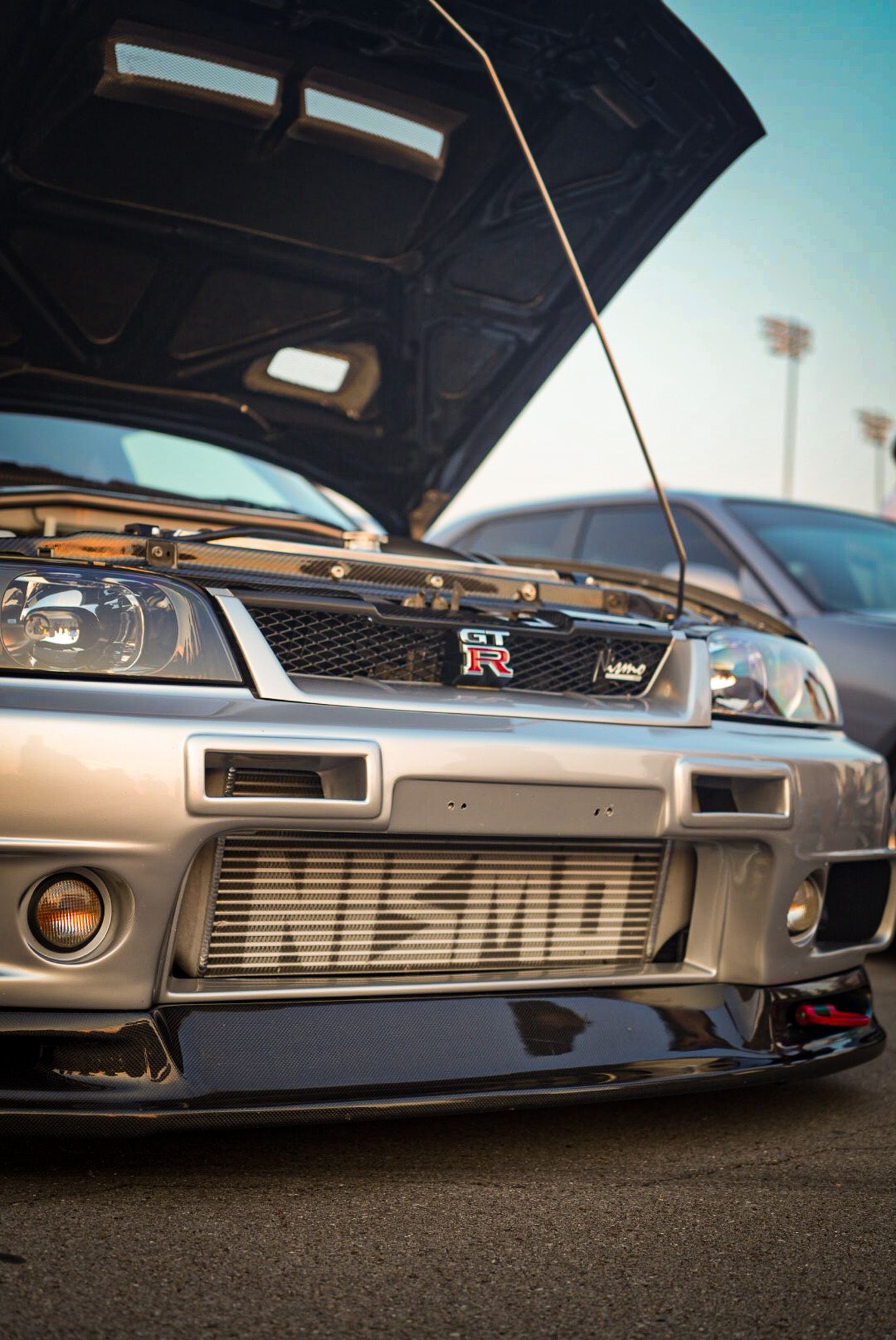 Nissan Skyline GT-R with NISMO front bumper and open hood displayed at a car meet. Cars & Christ