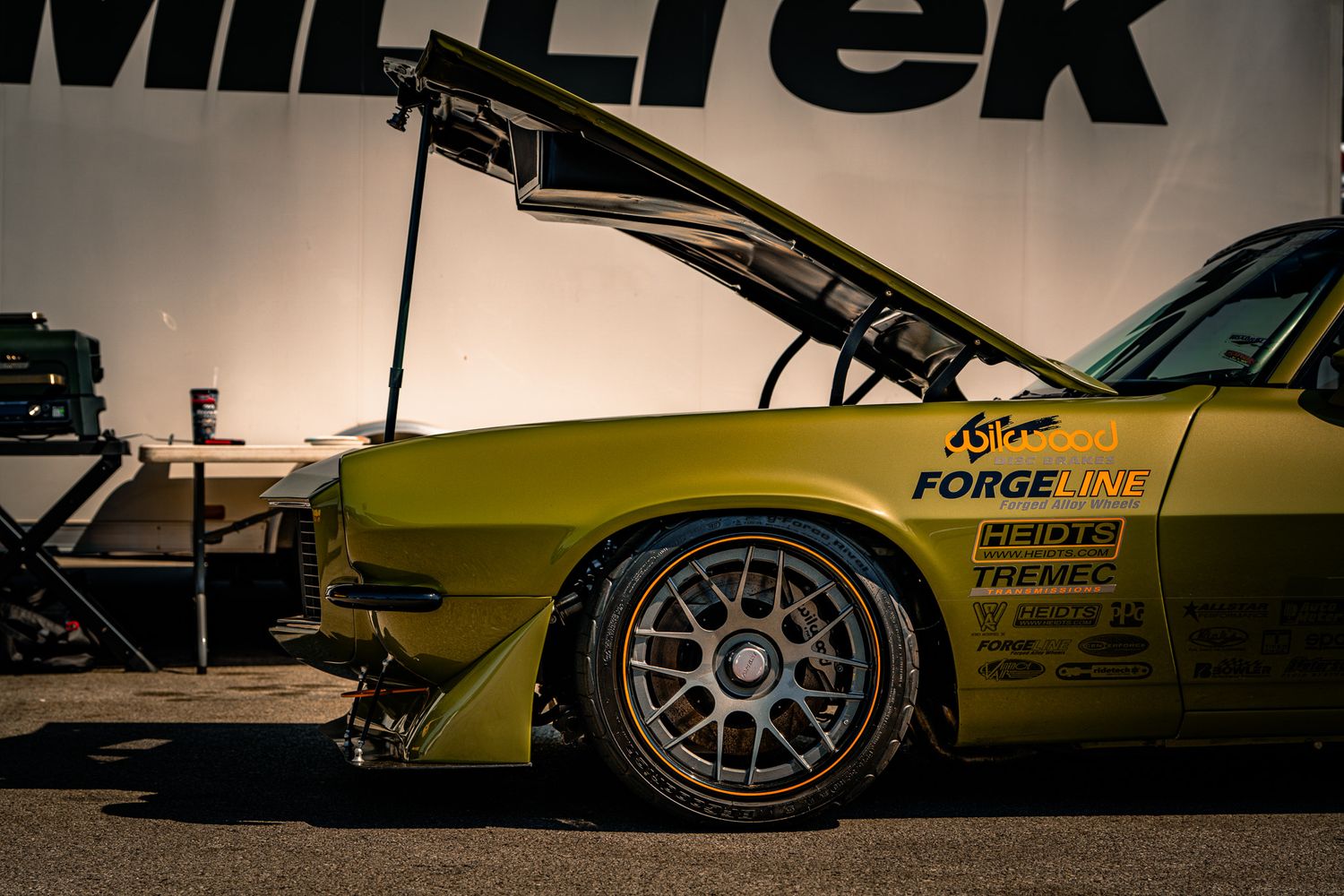 Yellow modified muscle car with Forgeline sponsorship decals and open hood at Milltek event. Holley LS Fest
