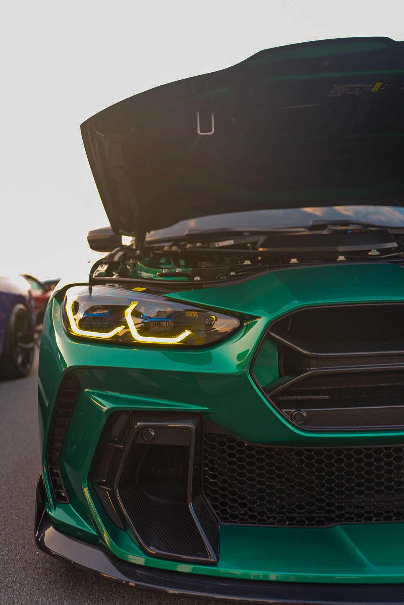 Green BMW M car with striking LED headlights and open hood displayed at an automotive event. Cars & Christ
