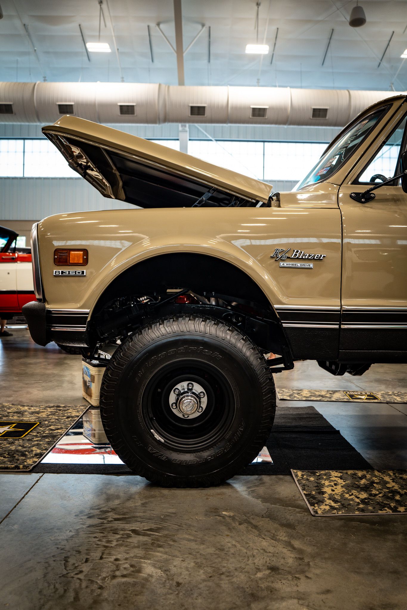 Lifted beige Chevy K5 Blazer with oversized off-road tires and open hood in garage. Southeastern Truck Nationals