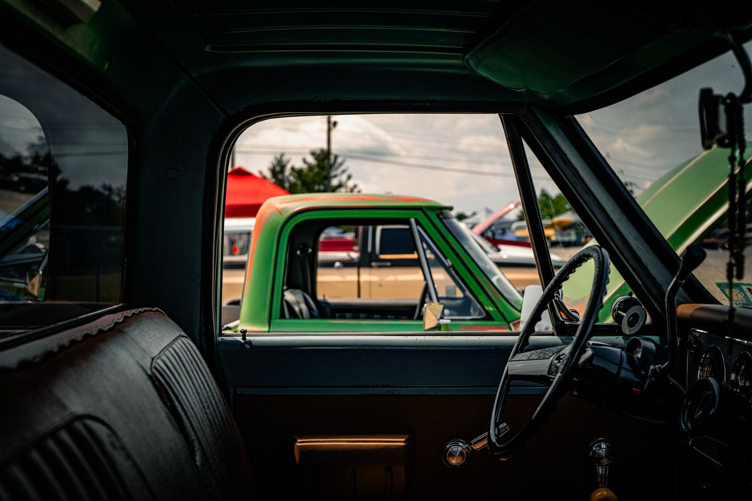 Interior view of a vintage green truck cab showing steering wheel and bench seat at a classic car show. GM Truck Fair