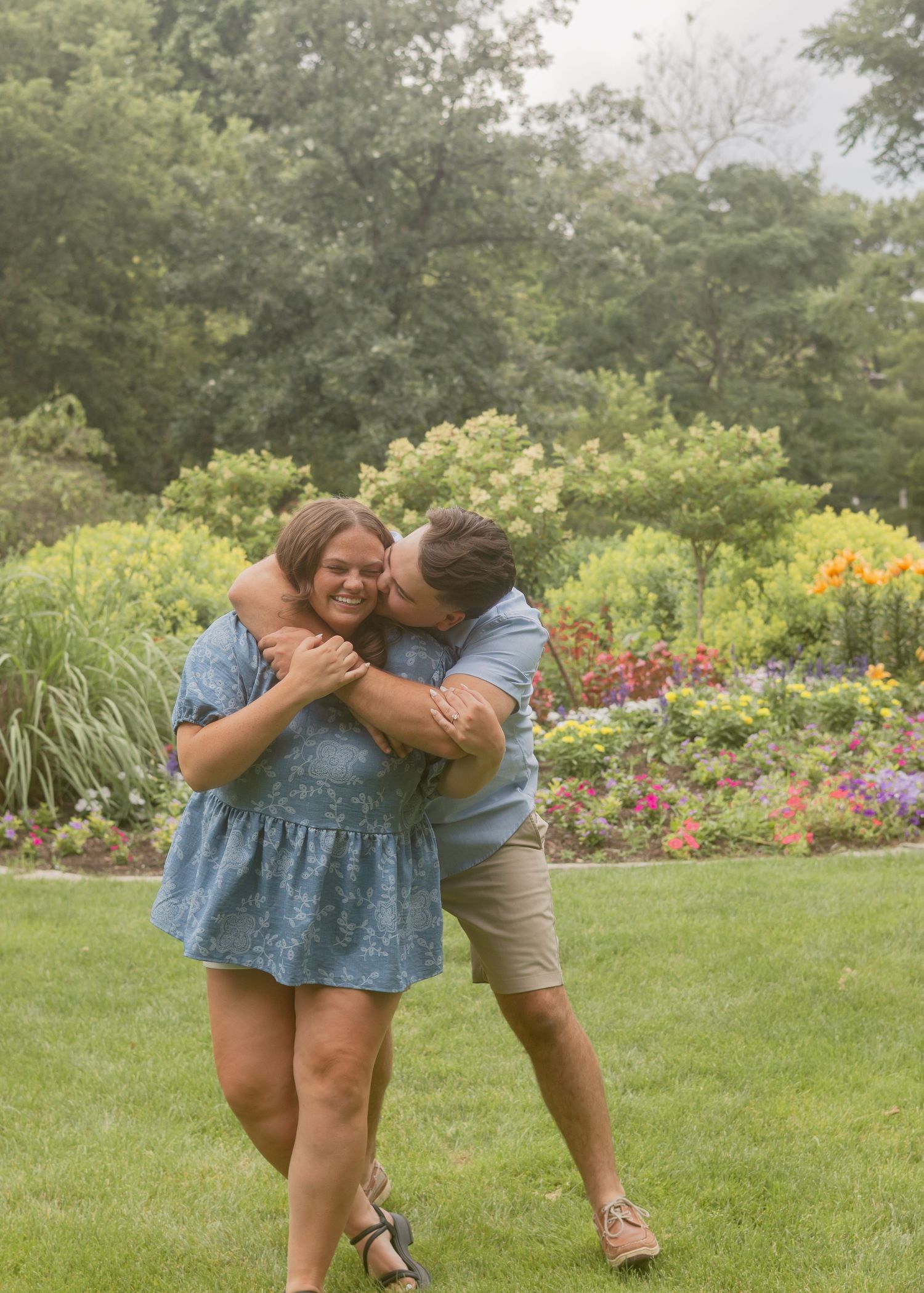 Joyful couple embracing and laughing together in front of vibrant colorful garden flower beds.