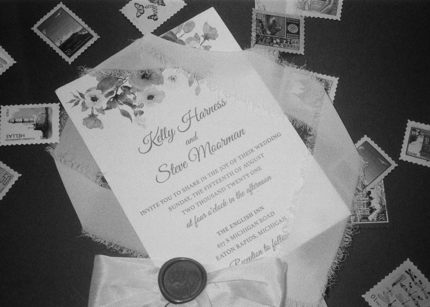 Black and white flat lay of a floral wedding invitation surrounded by vintage postage stamps.