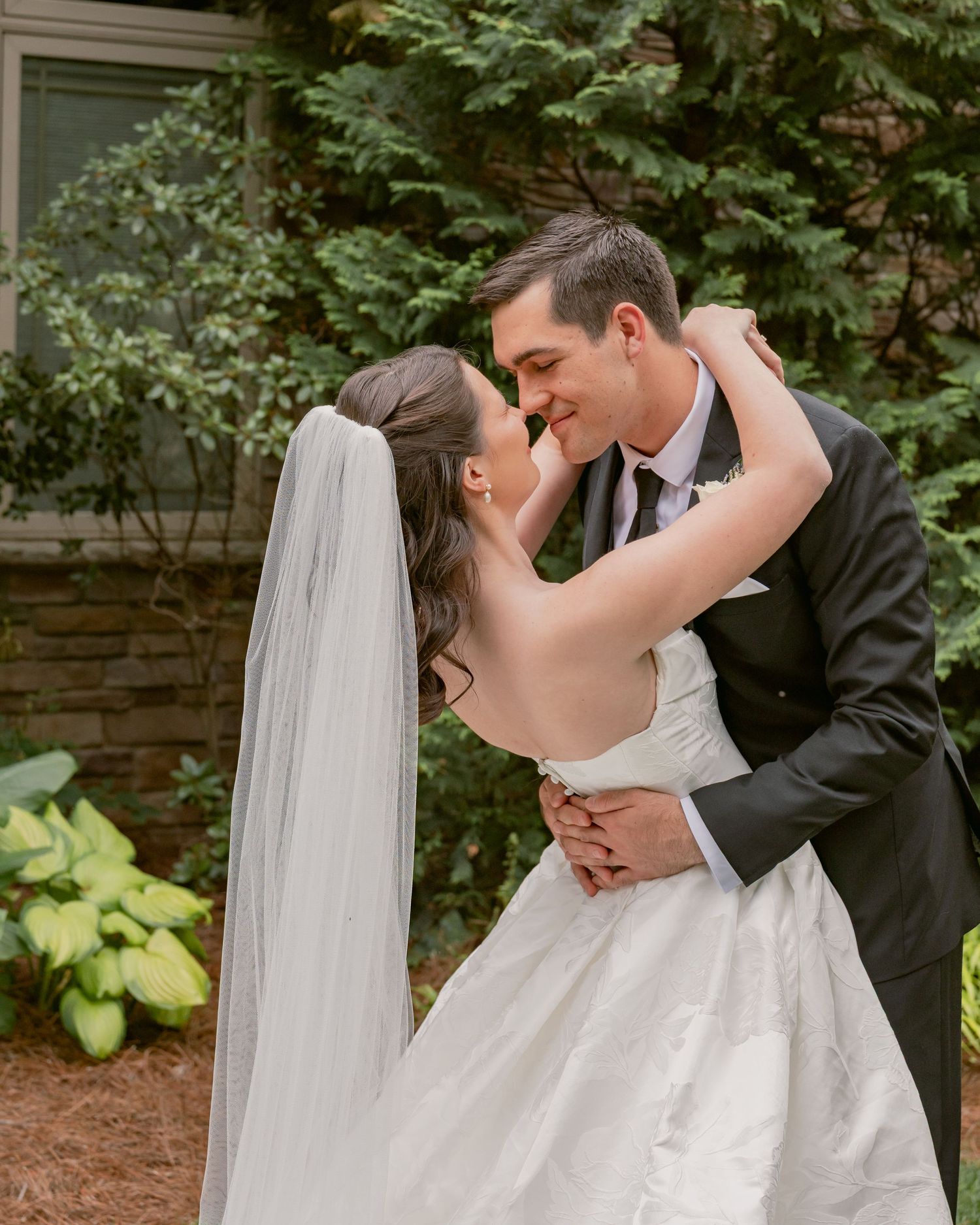 Bride and groom embrace and smile at each other in lush garden setting on their wedding day.