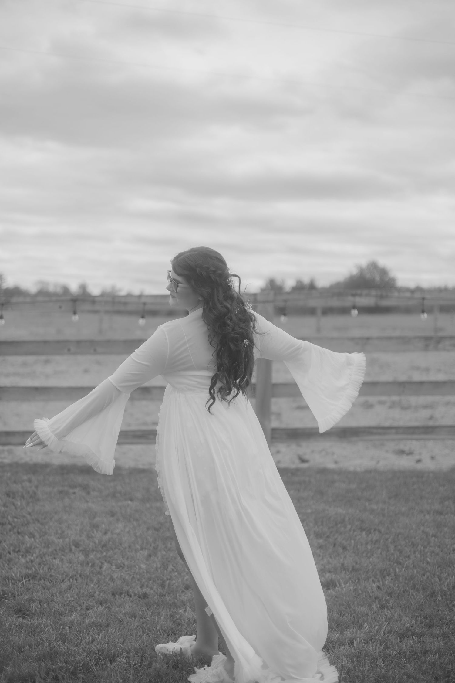 Black and white photo of bride in flowing white bell sleeve dress twirling gracefully outdoors.