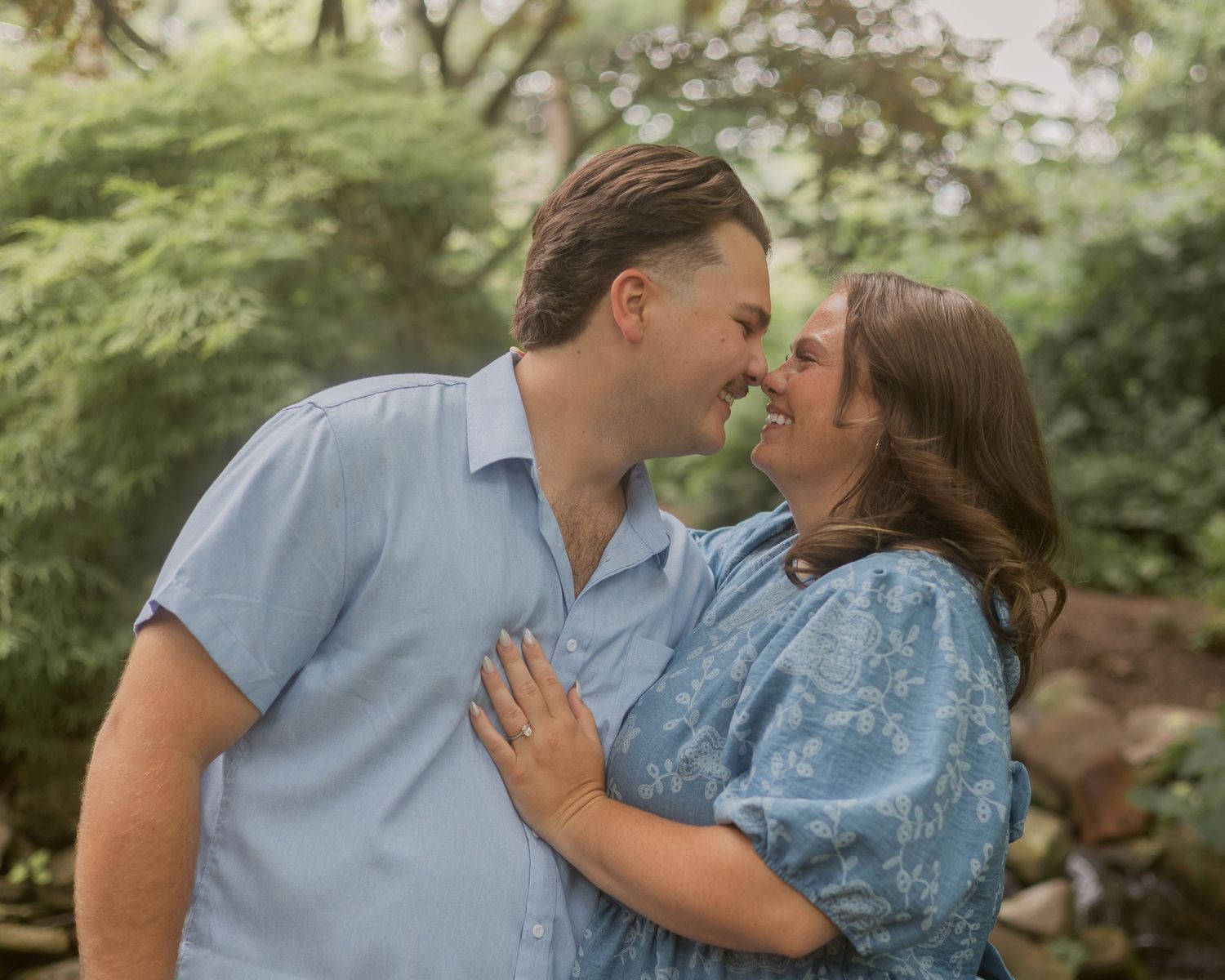 Happy couple sharing a romantic nose-to-nose moment surrounded by lush green garden foliage.