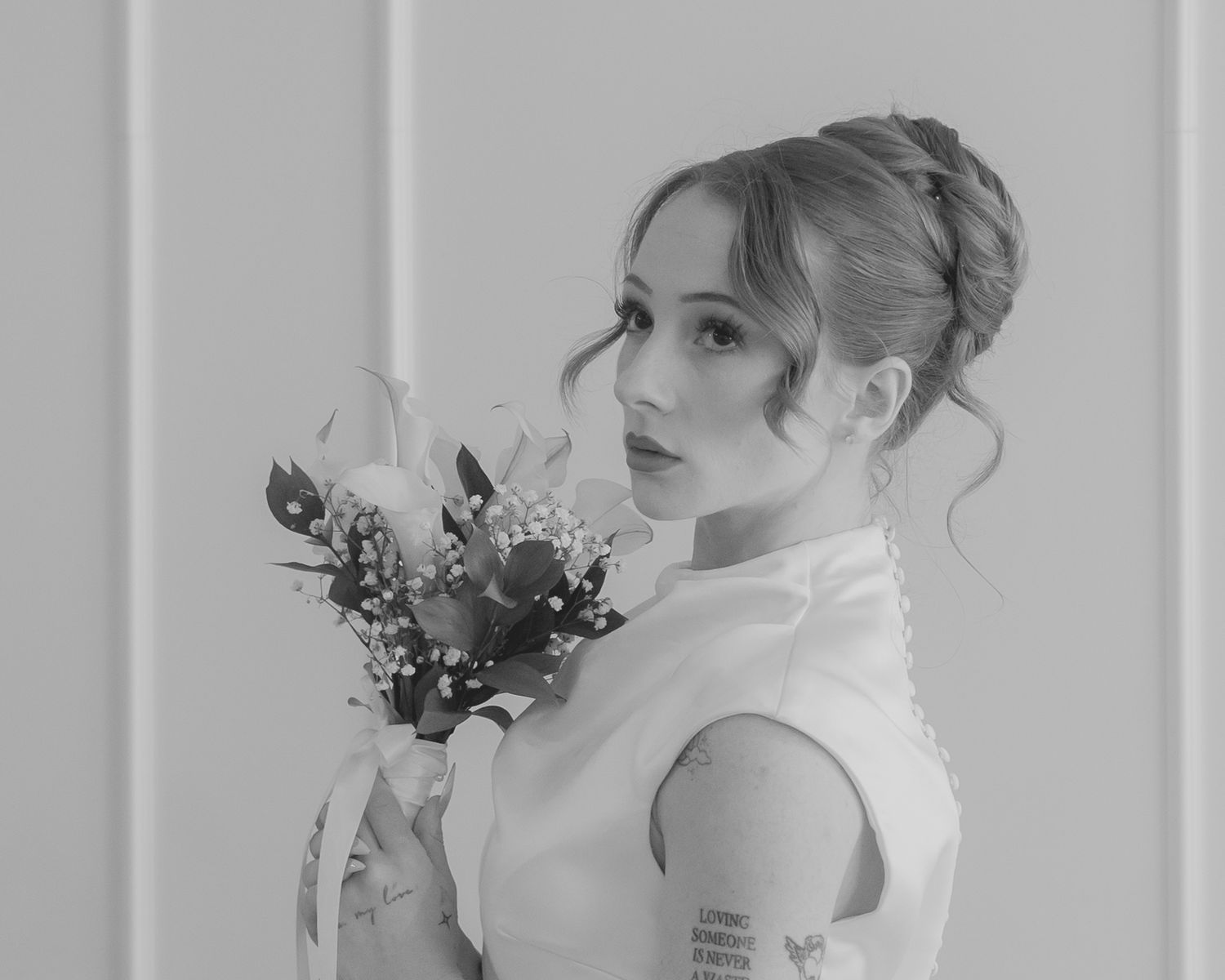 Black and white bridal portrait of elegant woman holding bouquet with updo hairstyle and tattoo.