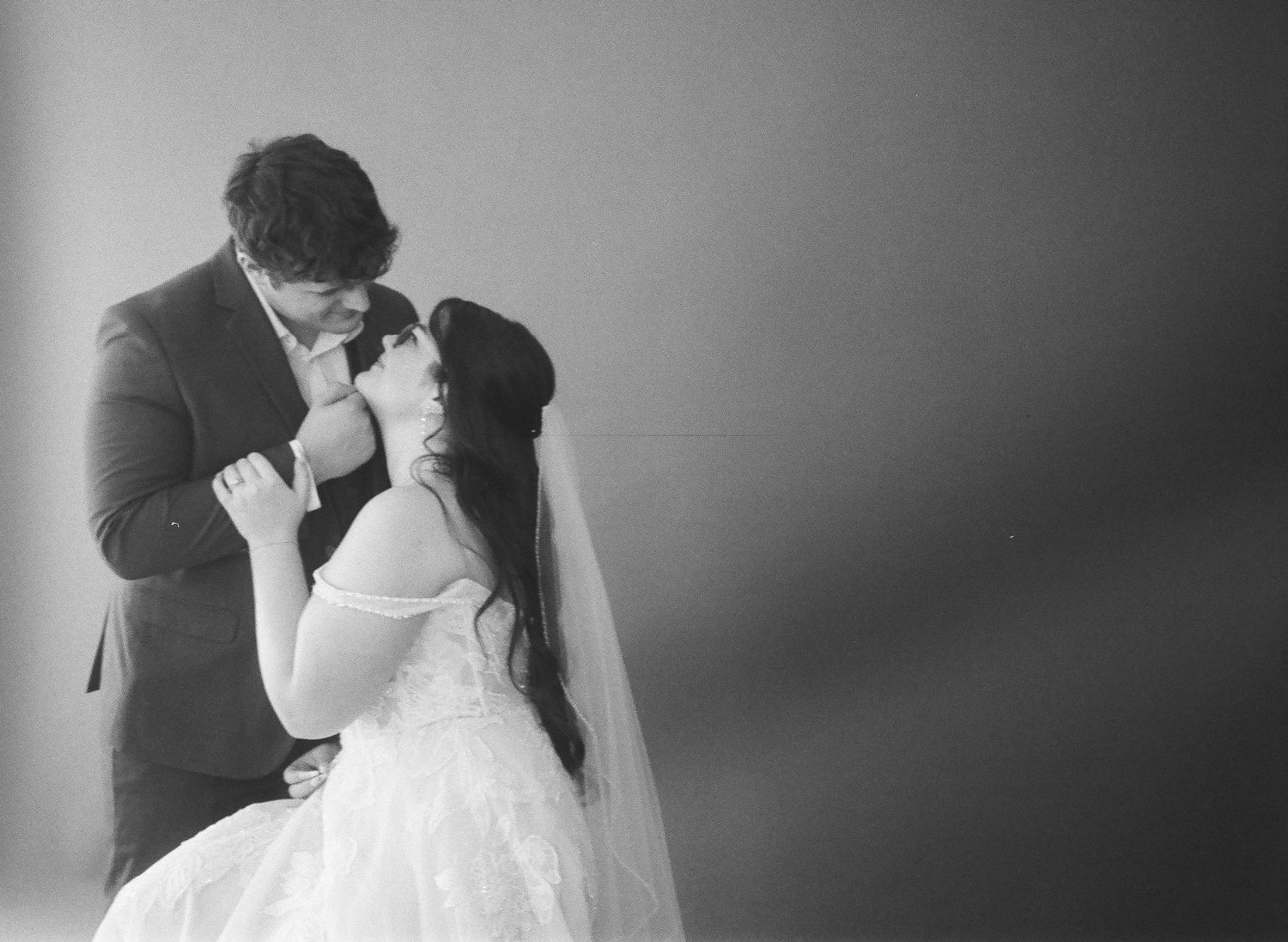 Black and white romantic photo of bride and groom sharing an intimate moment, groom kissing bride's hand tenderly.