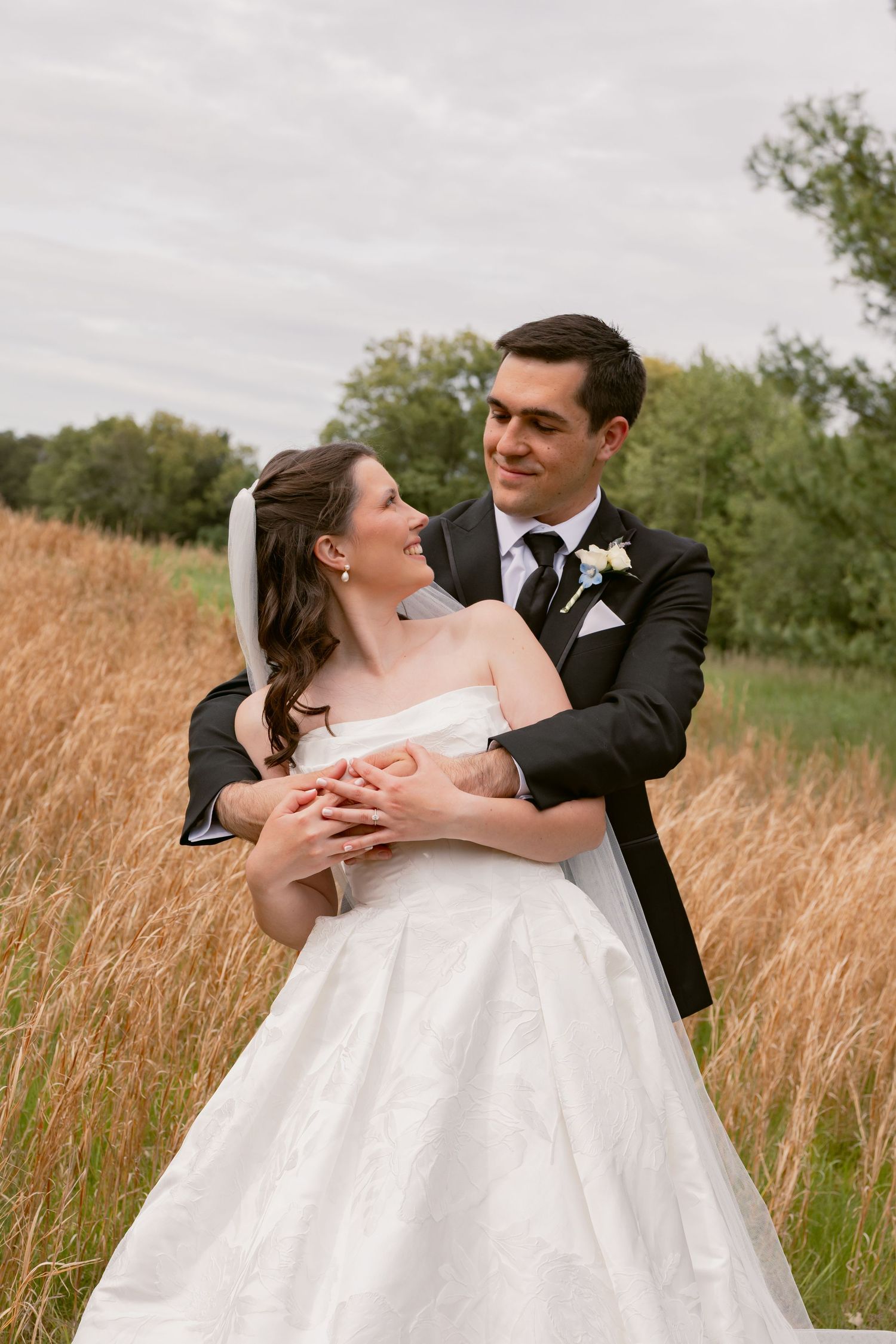 Groom embracing bride from behind in a golden wheat field, sharing a joyful romantic moment outdoors.